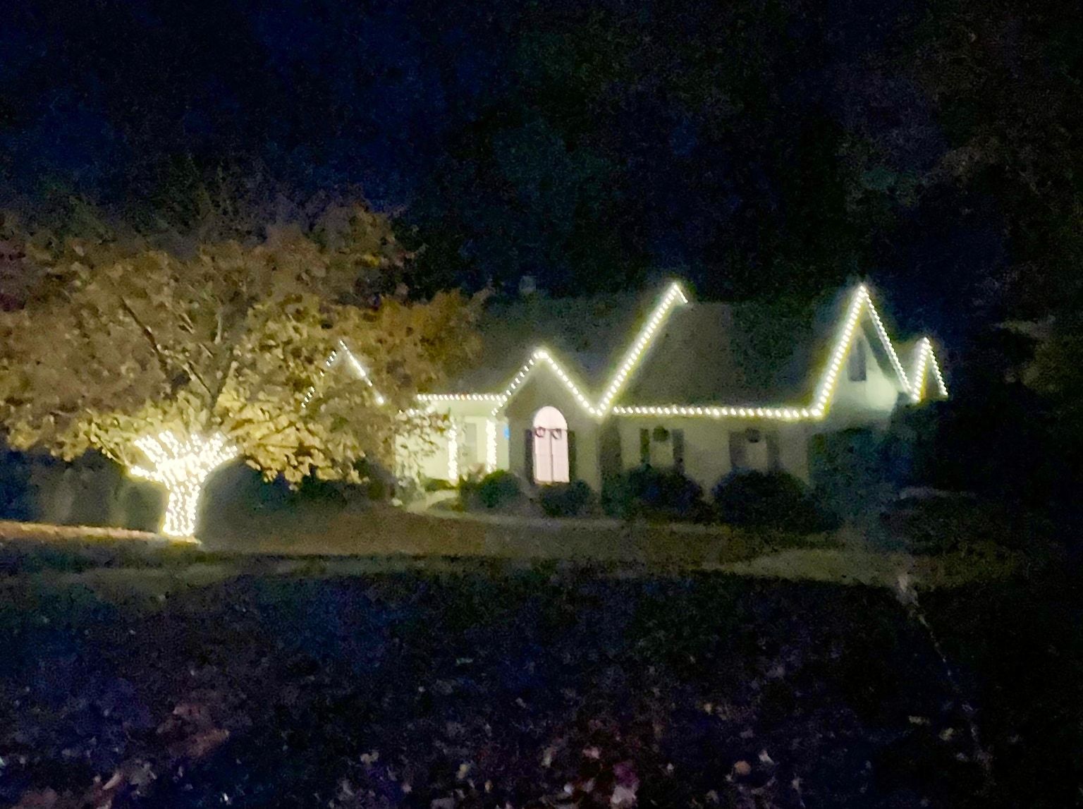 Warm white roofline lights on a multi-gable home with a wrapped tree trunk in the front yard